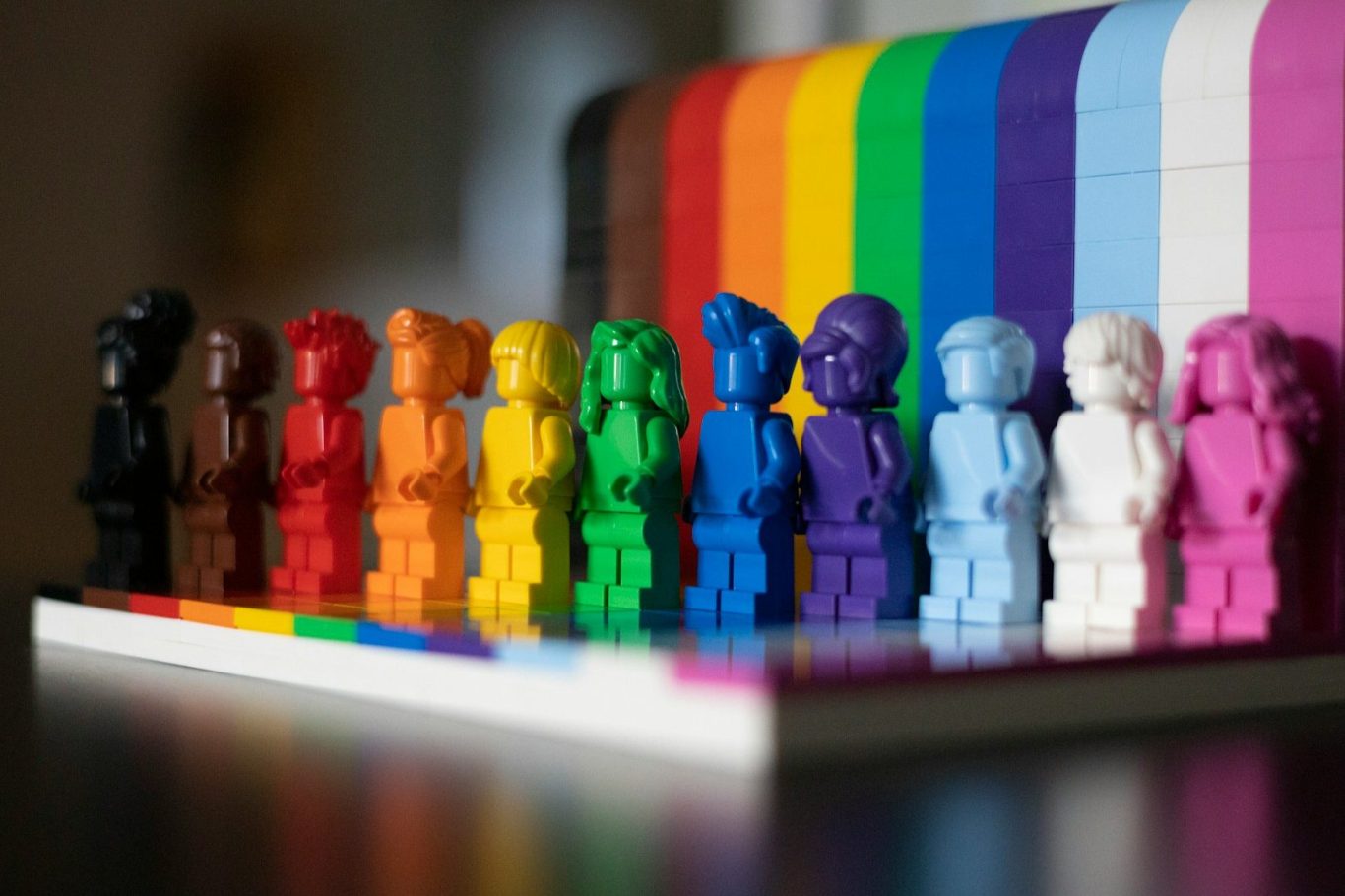 Bunte, LEGO-ähnliche Figuren in einer Reihe vor einem Regenbogen-Hintergrund.